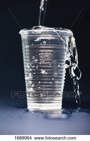 Picture - Close-up of water pouring in overflowing glass on table against black background. Fotosearch