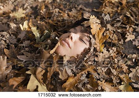 Stock Image - Close-up of woman with closed eyes covered in dry leaves. Fotosearch
