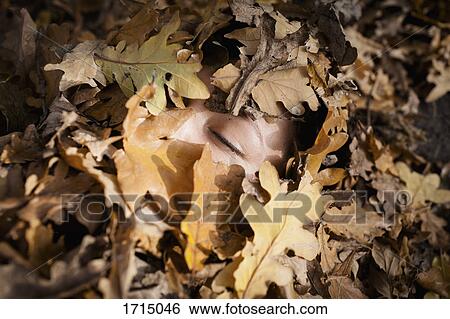Stock Photograph - Close-up of woman with closed eyes covered in dry leaves during autumn. Fotosearch