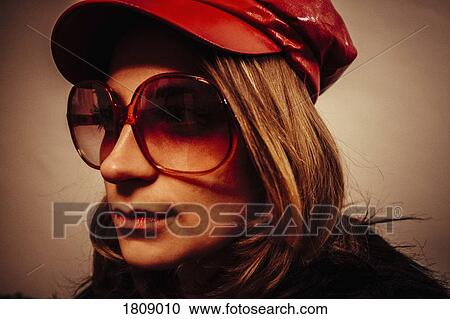 Stock Image - Close up portrait cool young woman wearing red leather cap and sunglasses. Fotosearch