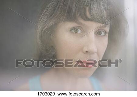 Stock Photo - Close-up portrait of mature woman seen from window glass. Fotosearch