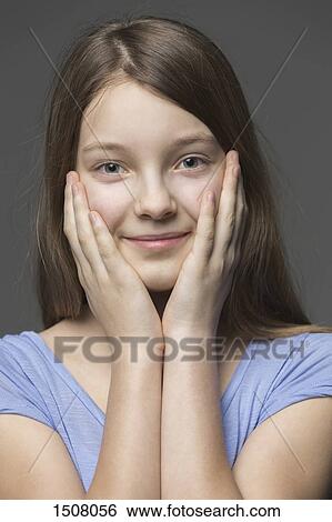 Stock Photograph - Close-up portrait of smiling girl with head in hands against gray background. Fotosearch