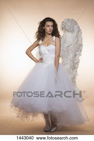 Confident bride in angel wings standing against colored background View Large Photo Image Stock Image - Confident bride in angel wings standing against colored background. Fotosearch