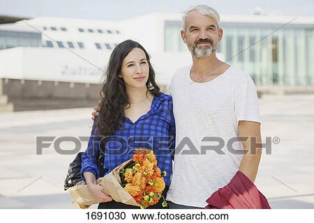 Confident couple with bouquet standing in city on sunny day View Large Photo Image Stock Image - Confident couple with bouquet standing in city on sunny day. Fotosearch