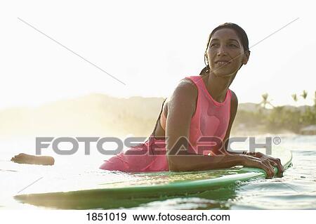 Confident female surfer leaning on surfboard in sunny ocean View Large Photo Image Stock Photo - Confident female surfer leaning on surfboard in sunny ocean. Fotosearch
