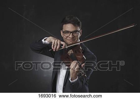 Confident smiling young man playing violin while standing against black background View Large Photo Image Stock Photograph - Confident smiling young man playing violin while standing against black background. Fotosearch