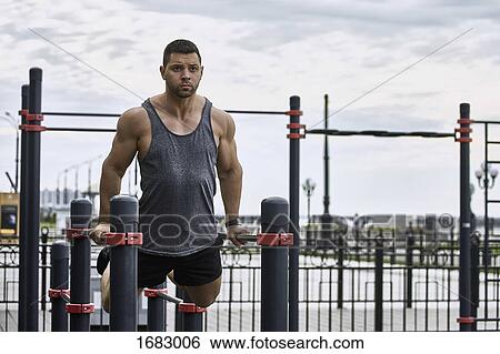 Confident young male athlete exercising on parallel bars against sky View Large Photo Image Stock Photograph - Confident young male athlete exercising on parallel bars against sky. Fotosearch