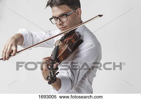Confident young man playing violin against white background View Large Photo Image Stock Photography - Confident young man playing violin against white background. Fotosearch