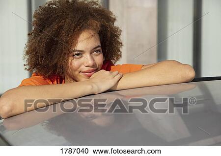 Stock Image - Confident young woman leaning on car. Fotosearch