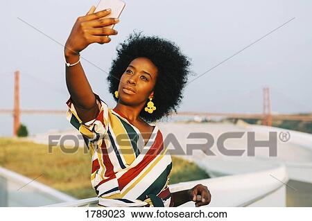 Confident young woman taking selfie with 25 de Abril Bridge in background, Lisbon, Portugal View Large Photo Image Stock Image - Confident young woman taking selfie with 25 de Abril Bridge in background, Lisbon, Portugal. Fotosearch