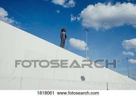 Stock Image - Cool, well-dressed young man with afro standing on sunny urban wall. Fotosearch