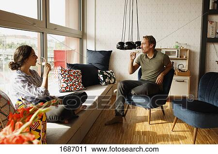 Couple drinking wine while sitting on window seat and chair at home View Large Photo Image Stock Image - Couple drinking wine while sitting on window seat and chair at home. Fotosearch