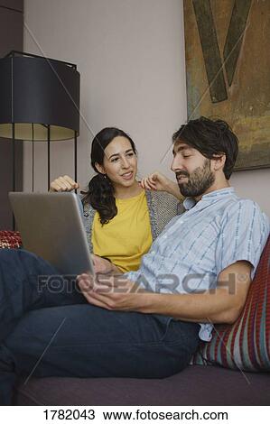 Stock Image - Couple using digital tablet on living room sofa. Fotosearch