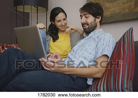 Stock Image - Couple using laptop on living room sofa. Fotosearch
