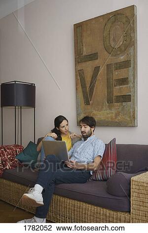 Stock Image - Couple using laptop on living room sofa. Fotosearch