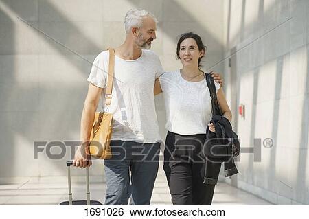 Couple with wheeled luggage walking at airport View Large Photo Image Stock Photograph - Couple with wheeled luggage walking at airport. Fotosearch