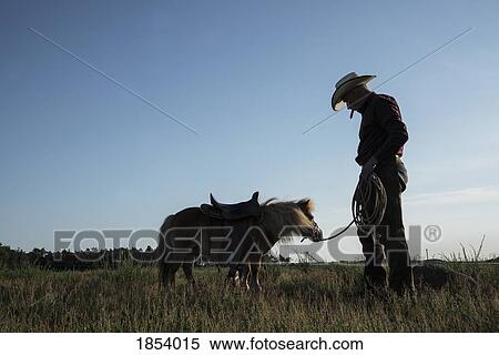Cowboy with saddled pony in sunny rural field View Large Photo Image Stock Photography - Cowboy with saddled pony in sunny rural field. Fotosearch