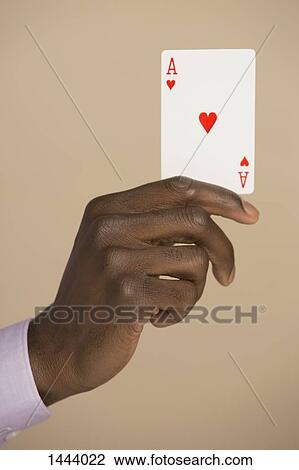 Stock Image - Cropped hand holding ace card against colored background. Fotosearch