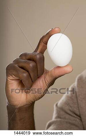 Stock Photo - Cropped hand holding egg against colored background. Fotosearch