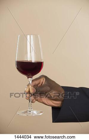 Cropped hand holding red wineglass against colored background View Large Photo Image Picture - Cropped hand holding red wineglass against colored background. Fotosearch