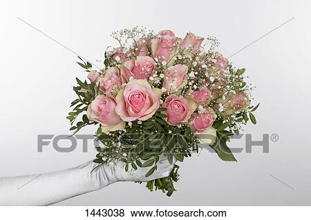 Stock Photo - Cropped hand of bride holding bouquet against white background. Fotosearch