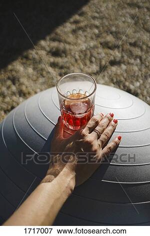 Stock Photo - Cropped hand of woman with drink on white exercise ball. Fotosearch
