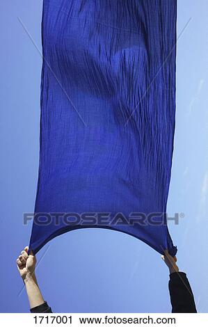 Stock Image - Cropped hands of woman holding blue sarong against clear sky. Fotosearch
