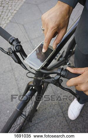 Stock Photography - Cropped image of businessman using mobile phone on bicycle handle while standing at street. Fotosearch