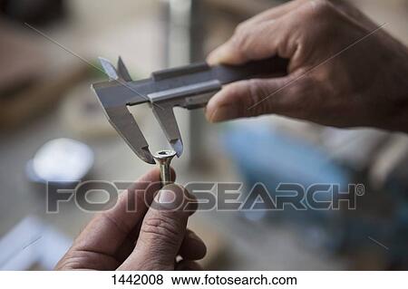 Stock Photo - Cropped image of carpenter measuring nail with caliper. Fotosearch