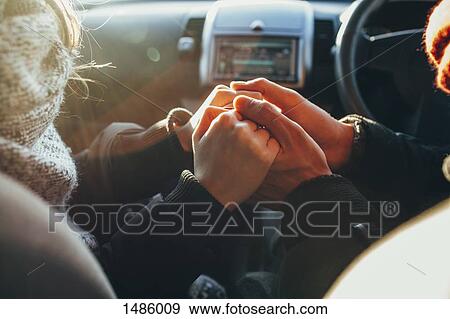 Stock Photo - Cropped image of couple holding hands in car. Fotosearch