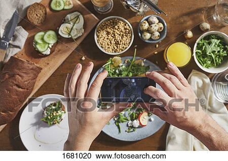 Stock Image - Cropped image of man photographing food on table with mobile phone. Fotosearch