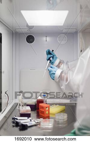 Stock Image - Cropped image of scientist holding pipette over machinery at laboratory. Fotosearch