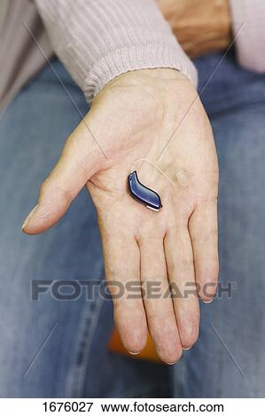 Stock Photo - Cropped image of senior woman holding hearing aid. Fotosearch