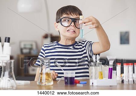 Stock Image - Cross eyed boy looking at test tube during science experiment in house. Fotosearch