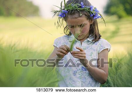 Curious girl with flowers in hair examining green wheat stalk in rural field View Large Photo Image Stock Photo - Curious girl with flowers in hair examining green wheat stalk in rural field. Fotosearch