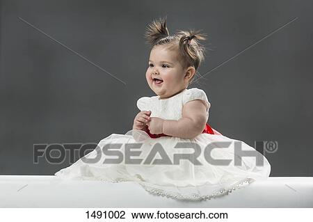 Stock Image - Cute baby girl wearing dress against gray background. Fotosearch