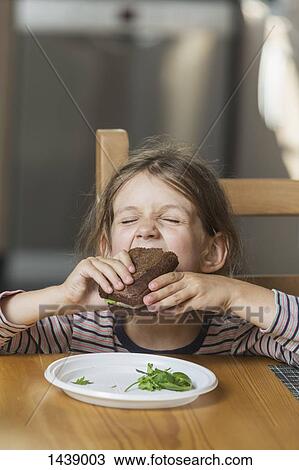 Cute girl eating sandwich at table in house View Large Photo Image Stock Image - Cute girl eating sandwich at table in house. Fotosearch