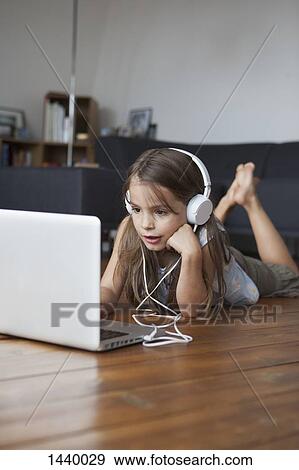 Cute girl listening music while using laptop on hardwood floor at home View Large Photo Image Stock Photo - Cute girl listening music while using laptop on hardwood floor at home. Fotosearch