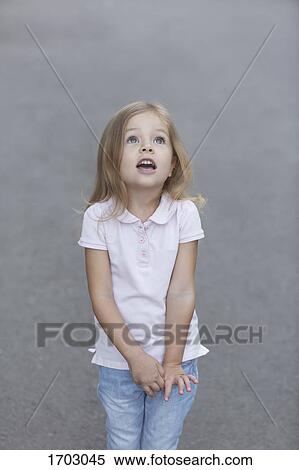 Cute girl looking up while standing against gray background View Large Photo Image Stock Photography - Cute girl looking up while standing against gray background. Fotosearch