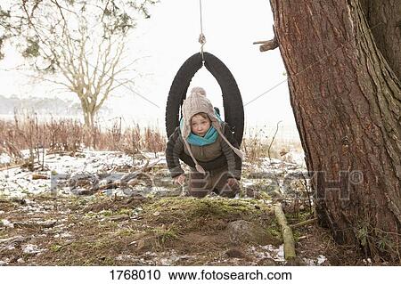 Stock Image - Cute girl playing in tire swing in snowy yard. Fotosearch