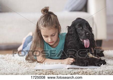 Cute girl reading book while lying by dog on rug at home View Large Photo Image Stock Photo - Cute girl reading book while lying by dog on rug at home. Fotosearch