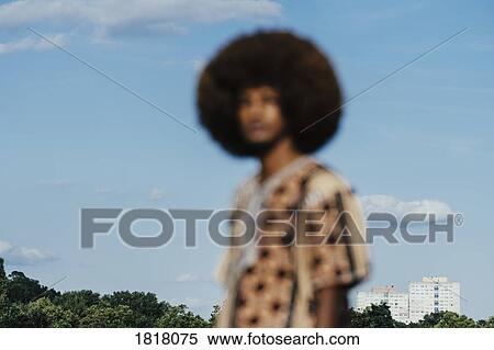 Stock Photography - Defocused portrait young man with afro standing against sunny blue sky. Fotosearch