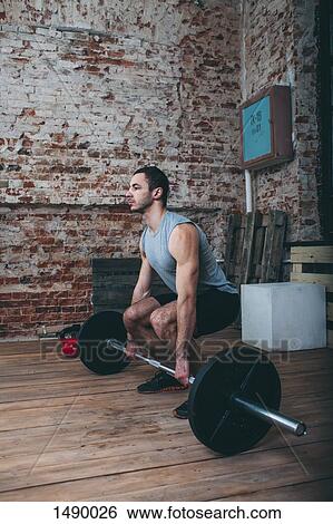 Determined young man lifting barbell at health club View Large Photo Image Stock Photograph - Determined young man lifting barbell at health club. Fotosearch