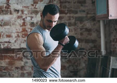 Determined young man lifting dumbbell at gym View Large Photo Image Stock Image - Determined young man lifting dumbbell at gym. Fotosearch