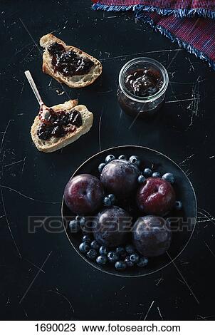 Stock Image - Directly above shot of fruits with open faced sandwich and preserves on granite. Fotosearch