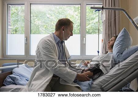 Doctor making rounds, checking blood pressure of patient in hospital room View Large Photo Image Stock Photo - Doctor making rounds, checking blood pressure of patient in hospital room. Fotosearch