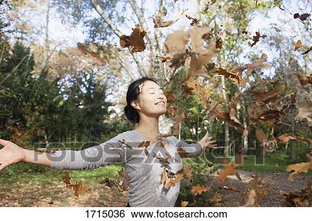 Dry leaves falling on happy woman standing with arms outstretched at park during autumn View Large Photo Image Stock Photograph - Dry leaves falling on happy woman standing with arms outstretched at park during autumn. Fotosearch