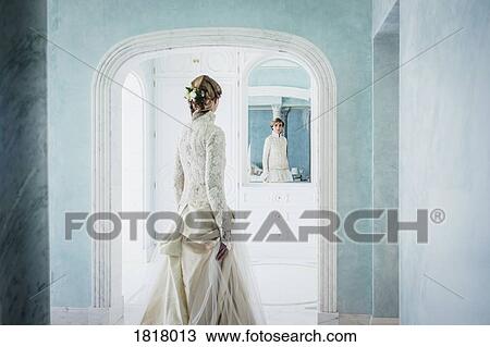 Stock Image - Elegant bride in lace wedding dress at mirror. Fotosearch
