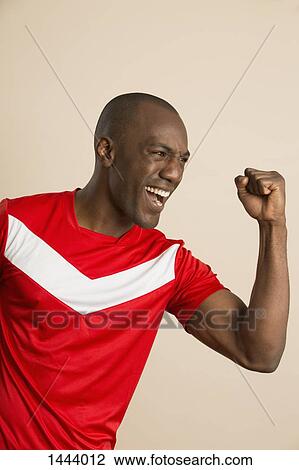 Stock Image - Enthusiastic soccer player with clenched fist against colored background. Fotosearch