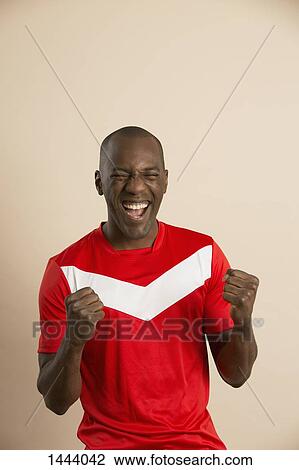 Stock Image - Excited soccer player screaming against colored background. Fotosearch